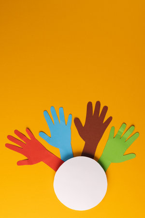 Paper cut out of multi coloured hands and white circle with copy space on orange background. Humanitarian aid, people, help and human concept.の写真素材
