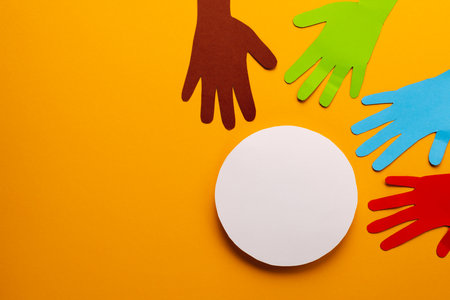 Paper cut out of multi coloured hands and white circle with copy space on orange background. Humanitarian aid, people, help and human concept.の写真素材