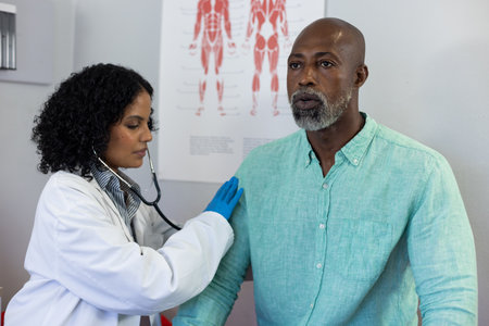 Biracial female doctor using stethoscope and examinating african american male patient. Hospital, medicine and healthcare.の写真素材