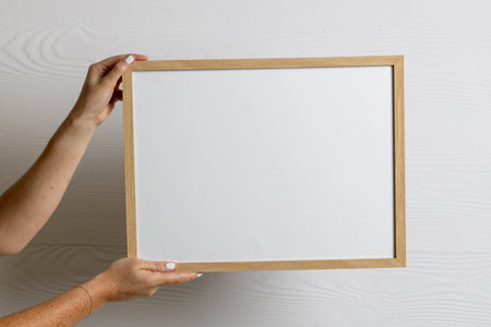 Hands holding wood empty frame with copy space against white wall. Mock up frame template, interior...