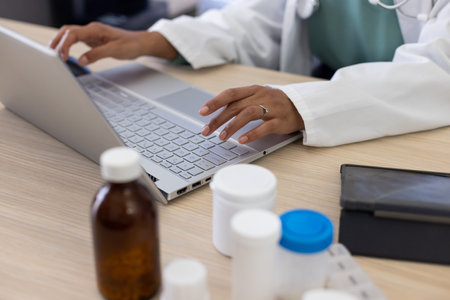 Midsection of biracial female doctor using laptop at doctor&#39;s office. Hospital, medicine, healthcare and communication.の写真素材