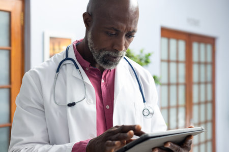 African american male doctor wearing stethoscope using tablet at doctor&#39;s office. Hospital, medicine, healthcare and communication.の写真素材