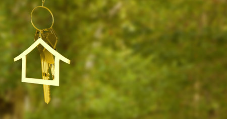 Image of house model and key hanging over defocused grassy field. Digital composite, new home, metallic, ownership, gold colored, moving, keyring.の写真素材