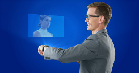 Composition of caucasian businessman using smartwatch displaying caucasian woman on blue background. Technology, computing and digital interface concept digitally generated image.の写真素材