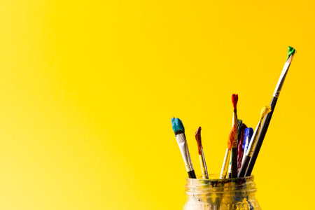Image of close up of jar with paint brushes and copy space on yellow background. Painting, arts and...