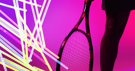 Midsection of african american male tennis player with racket by glowing lines on pink background. Copy space, composite, sport, competition, neon, leg, illuminated and abstract concept.の写真素材