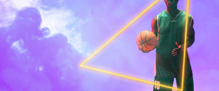 Midsection of african american male player with basketball by glowing triangle on smoky background. Copy space, composite, illuminated, sport, competition, illustration, shape and abstract concept.の写真素材