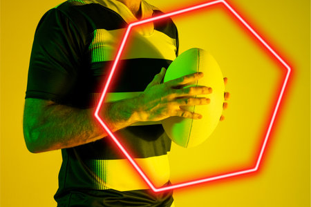 Illuminated hexagon over midsection of caucasian male player holding rugby ball on yellow background. Copy space, composite, sport, competition, shape, playing, match, hand and abstract concept.の写真素材