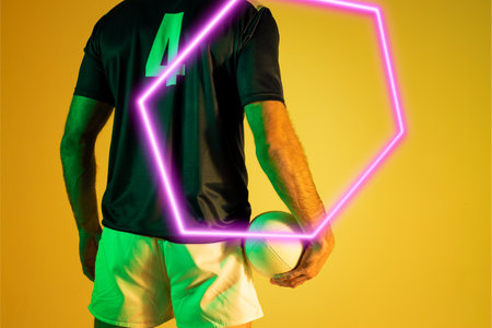 Illuminated hexagon over rear view of caucasian male player with rugby ball on yellow background. Copy space, composite, sport, competition, shape, playing, match, hand and abstract concept.の写真素材