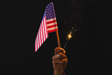 Hand of biracial man holding flag of united states of america and sparkler with copy space. American patriotism, independence day and tradition concept.の写真素材