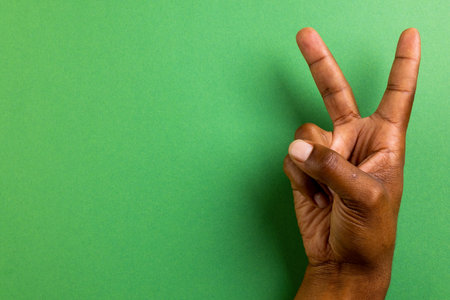 Close up of hand of biracial man showing peace sign with copy space on green background. Peace and anti war movement concept.の写真素材