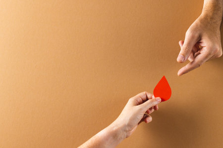 Hands of caucasian woman passing blood drop to caucasian man, on brown background with copy space. Blood donation, medicine and healthcare.の写真素材