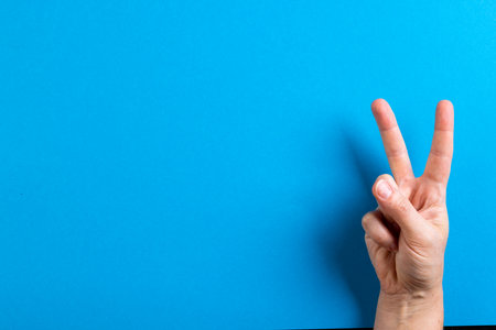 Close up of hand of caucasian woman showing peace sign with copy space on blue background. Peace and anti war movement concept.の写真素材