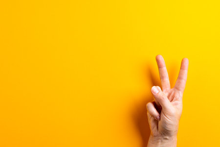 Close up of hand of caucasian woman showing peace sign with copy space on yellow background. Peace and anti war movement concept.の写真素材