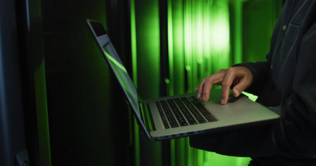 Composition of green light over african american businessman using laptop in server room. Technology, computing and online security concept digitally generated image.の写真素材