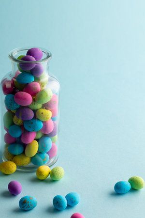 Image of multi coloured easter eggs in clear jar with copy space on blue background. Easter,...