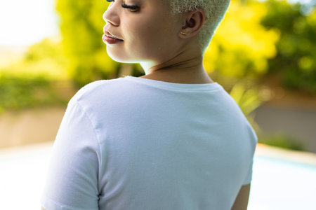 Close up of biracial woman wearing white tshirt over swimming pool in garden. Clothing, material and model.の写真素材