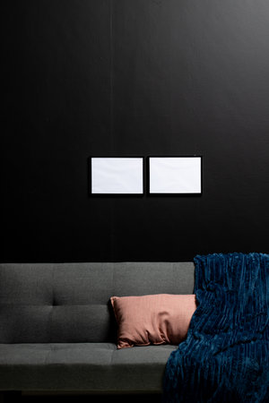 Vertical of empty white canvases with copy space on black wall in room with couch. Mock up frame...