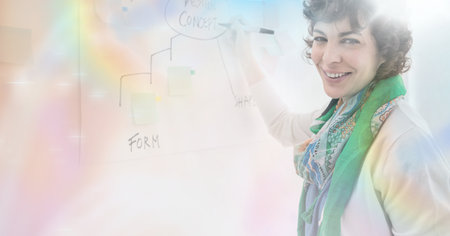 Composition of smiling businesswoman writing on whiteboard in office over glowing light trails. business, finances, success and communication concept digitally generated image.の写真素材