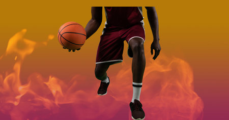 Composition of low section of male basketball player holding ball, over flames on orange background. sport and competition concept digitally generated image.の写真素材