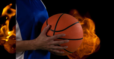 Composition of midsection of male basketball player holding ball over flames on black background. sport and competition concept digitally generated image.の写真素材