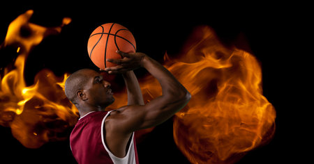 Composition of male basketball player shooting with ball over flames on black background. sport and competition concept digitally generated image.の写真素材