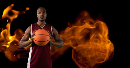 Composition of male basketball player standing holding ball over flames on black background. sport and competition concept digitally generated image.の写真素材