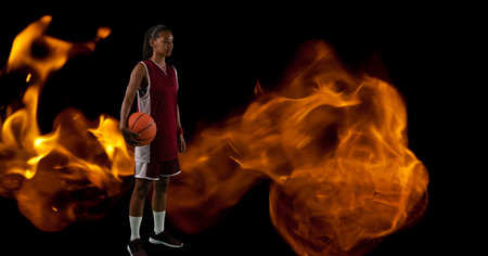 Composition of male basketball player standing holding ball over flames on black background. sport and competition concept digitally generated image.の写真素材