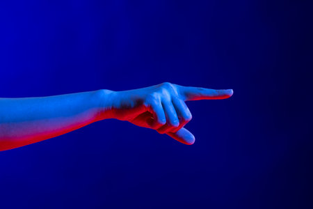 Exposed hand pointing finger in studio with blue light with copy space. Virtual reality and digital interface technology.の写真素材