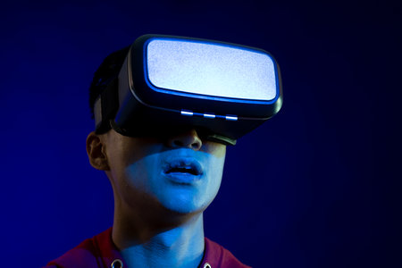 Asian man using vr headset in studio with blue light with copy space. Virtual reality and digital...