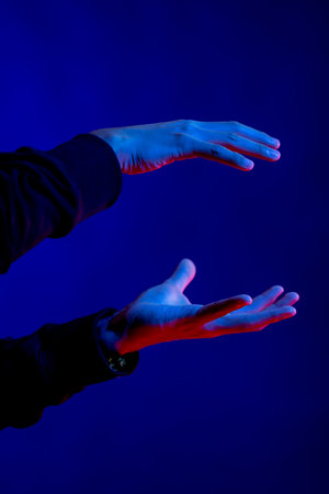 Exposed hands making gestures in studio with blue light with copy space. Virtual reality and digital interface technology.の写真素材