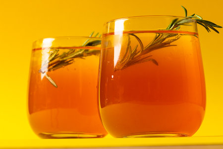 Glasses with drinks and thyme over yellow background. Drinks, cocktails, alcohol, beverages and party concept.の写真素材