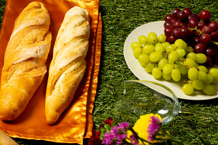 Bread loafs, grapes, glass and flowers lying on grass. Picnic, food, eating outside, relaxing in nature concept.の写真素材