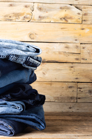 Vertical image of diverse folded jeans in stack over wooden background. Clothes, fashion, design, fabrics, materials and shopping concept.の写真素材