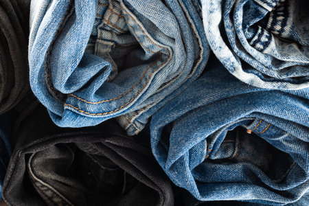 Close up of diverse folded jeans lying in stack on white background. Clothes, fashion, design, fabrics, materials and shopping concept.の写真素材