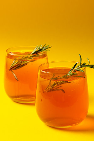 Vertical image of glasses with drinks and thyme over yellow background. Drinks, cocktails, beverages and party concept.の写真素材
