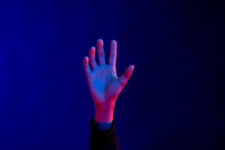 Asian man with open hand in studio with blue light with copy space. Virtual reality and digital...