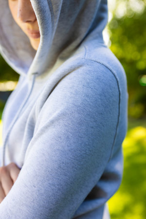 Close up of caucasian woman wearing gray hoodie over green park on sunny day. Clothing, material and model.の写真素材