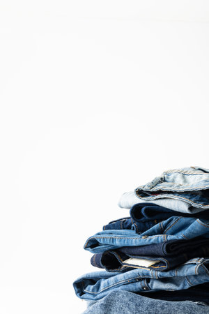 Vertical image of diverse folded jeans lying in stack on white background. Clothes, fashion, design, fabrics, materials and shopping concept.の写真素材