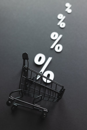 Shopping trolley and white percent signs with copy space on grey background. Black friday, cyber...