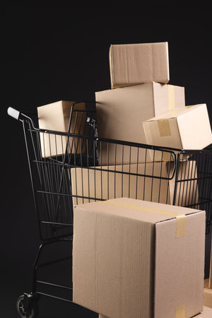 Vertical image of shopping trolley with boxes and copy space over black background. Cyber monday, black friday, online shopping, shipping and global connections concept.の写真素材