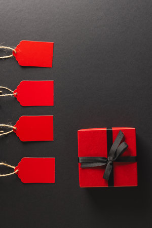 Vertical image of red gift tags and red gift box with copy space over black background. Cyber monday, black friday, online shopping, shipping and global connections concept.の写真素材