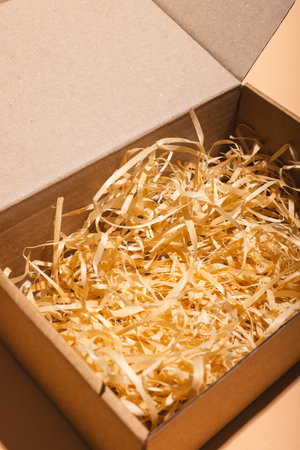 Vertical image of open box with straw lining and copy space over cream background. Cyber monday, black friday, online shopping, shipping and global connections concept.の写真素材