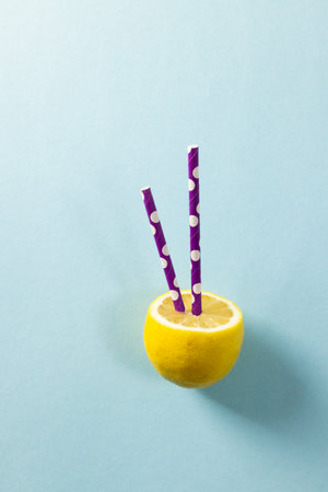 Close-up of fresh lemon with violet drinking straws against blue background, copy space. Yellow, citrus fruit, food, lemonade, healthy concept.の写真素材