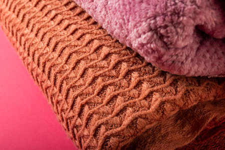 Close-up of brown and pink sweaters stacked and arranged on pink background, copy space. Warm...