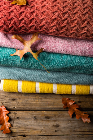 High angle view of multicolored sweaters stacked with leaves on wooden table. Unaltered, nature,...