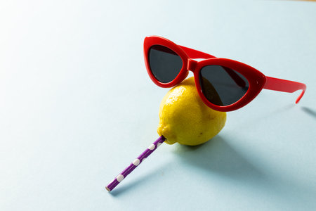 High angle view of lemon with sunglasses and drinking straw arranged on blue background, copy space. Summer, protection, refreshment, citrus fruit, food, healthy concept.の写真素材