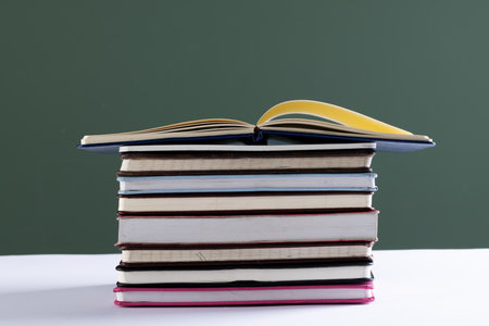 Close up of stack of books and notebooks with copy space on green background. Reading, learning,...