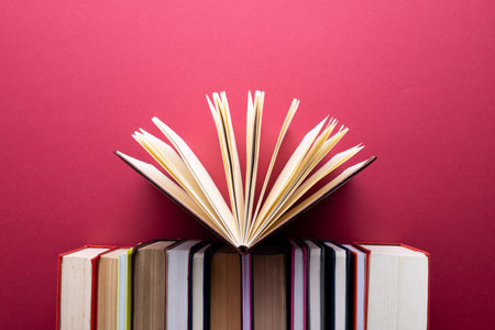 Books and notebooks in row with opened notebook on top and copy space on red background. Reading, learning, school and education concept.の写真素材