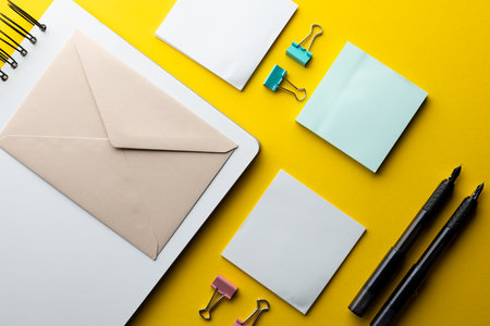 Flat lay of black pens, envelope and white paper with copy space on yellow background. School...
